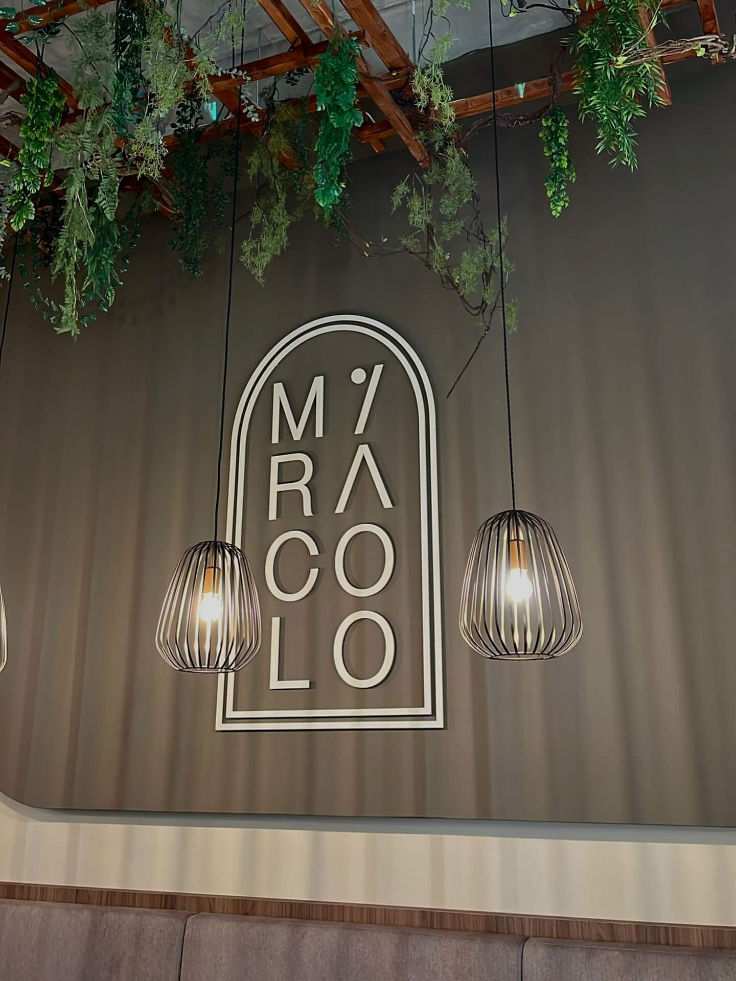 Wand met het logo van restaurant Miracolo, hangplanten en twee kooivormige hanglampen.