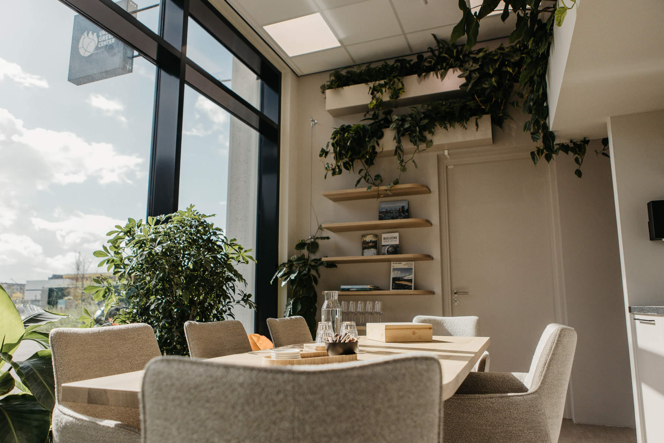 Lounge met een ronde tafel, planten en boekenplanken, met zicht op het Urban Green Center.