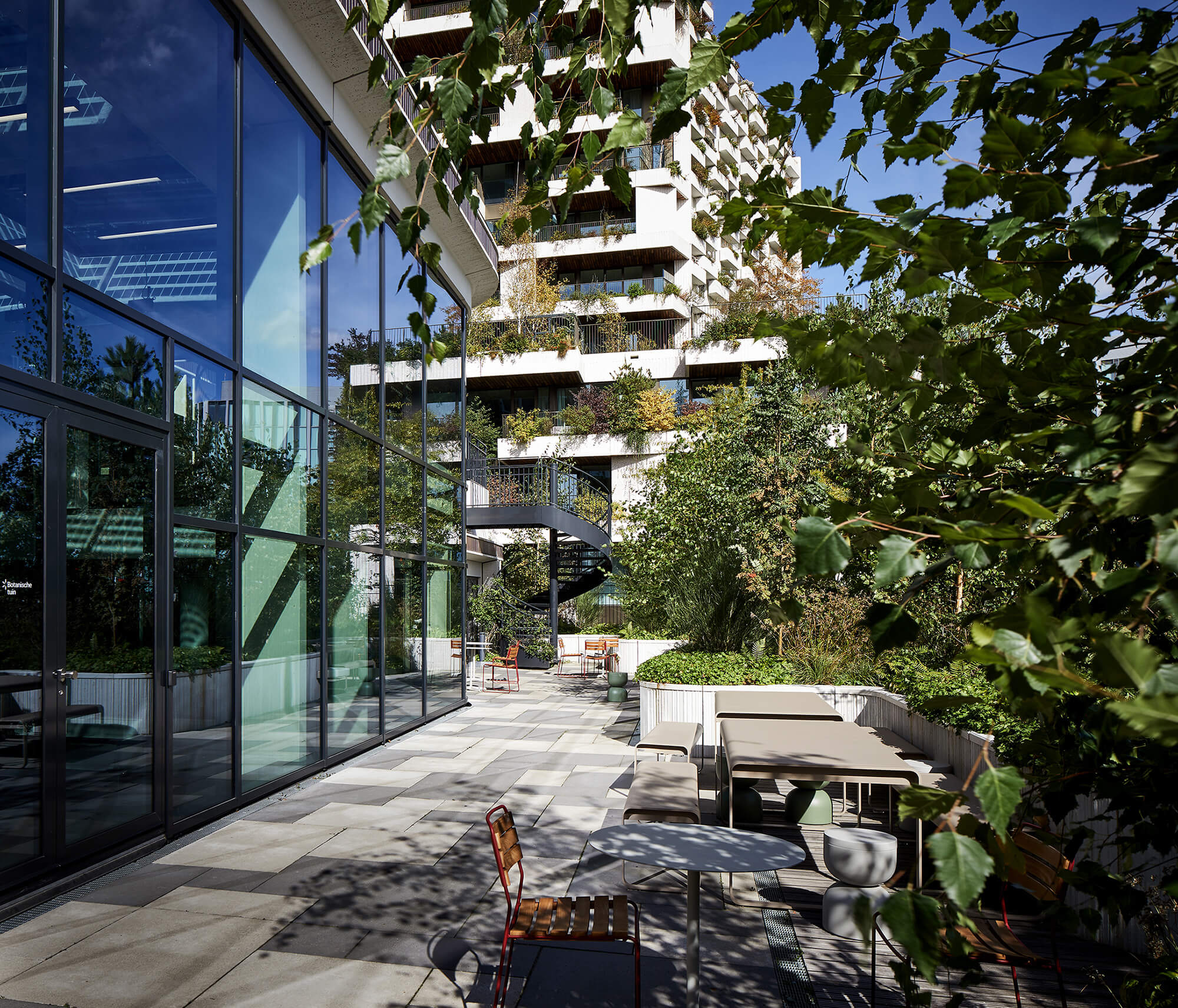 Dakterras van Wonderwoods met buitenmeubilair en een wenteltrap, met de beplante balkons van de toren op de achtergrond.